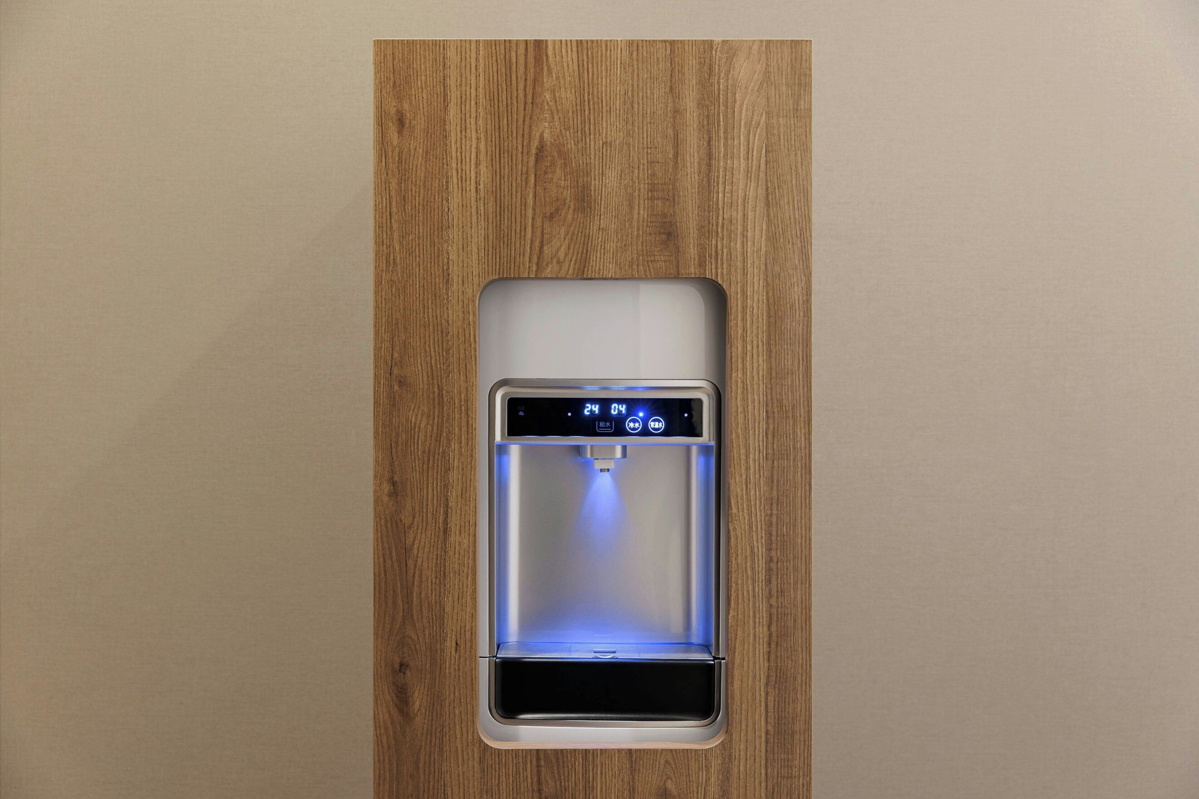 Een waterdispenser, ingebouwd in een houten paneel, met een digitaal scherm dat de tijd weergeeft.