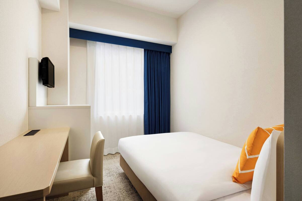 Ett hotellrum med en säng, ett skrivbord, en stol och ett fönster med gardiner.