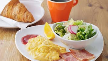 Un plat amb ous remenats, bacon, un croissant, un bol de amanida amb rave i una làmina de taronja.