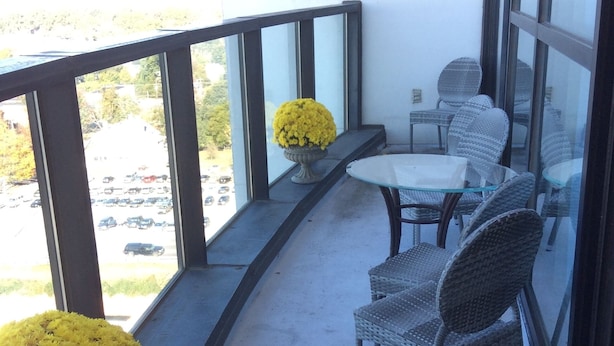 Un balcon avec des fauteuils en osier et une table, un pot de fleurs contenant des fleurs jaunes, et une vue sur un parking.