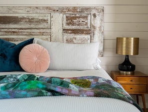 A bed with a colorful blanket, a headboard with a distressed wood finish, and a bedside table with a lamp. - Romantic Fredericksburg Cottage w/ Hot Tub (Fredericksburg)