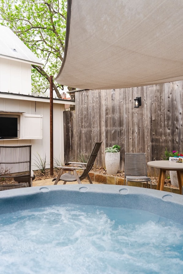 A backyard with a hot tub, a wooden fence, a chair, a table, and a potted plant. - Romantic Fredericksburg Cottage w/ Hot Tub (Fredericksburg)