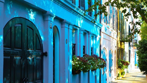 Una hilera de edificios con ventanas y puertas arqueadas, algunos adornados con macetas colgantes de flores.