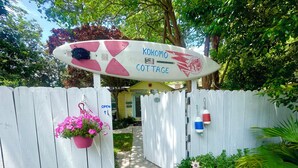 Una verja de madera con un letrero que dice "Kokomog Cottage" y una cesta de flores rosadas colgada a la izquierda.