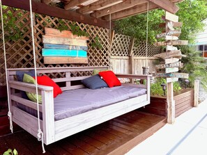 A wooden swing bed with cushions, a wooden lattice wall, and a signpost with destination names.