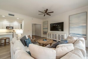 A modern living room with a white sofa, a wooden coffee table, and a ceiling fan.