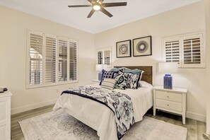 A bedroom with a bed, nightstands, a ceiling fan, and wall-mounted artwork.