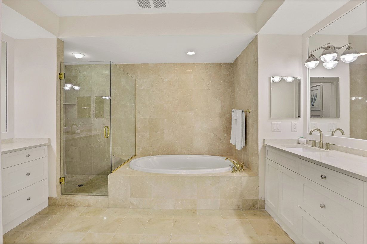 A modern bathroom with a glass-enclosed shower, a freestanding bathtub, and a vanity with a large mirror and lights.