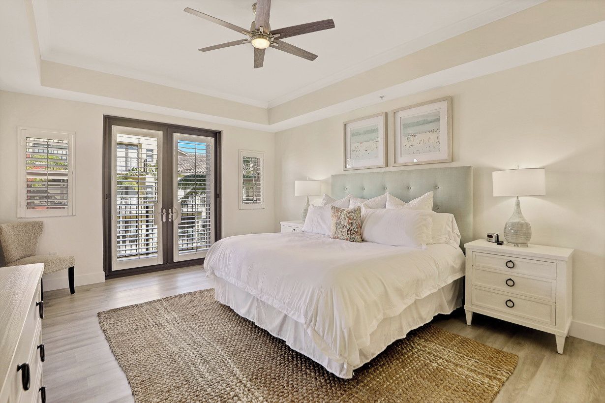 A bedroom with a large bed, a ceiling fan, a nightstand, and a view through the glass doors.