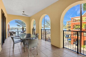 A balcony with a table and chairs, arched windows, and a view of palm trees and buildings. - Luxurious Esplanade Condo | Overlooking Bay (Marco Island)