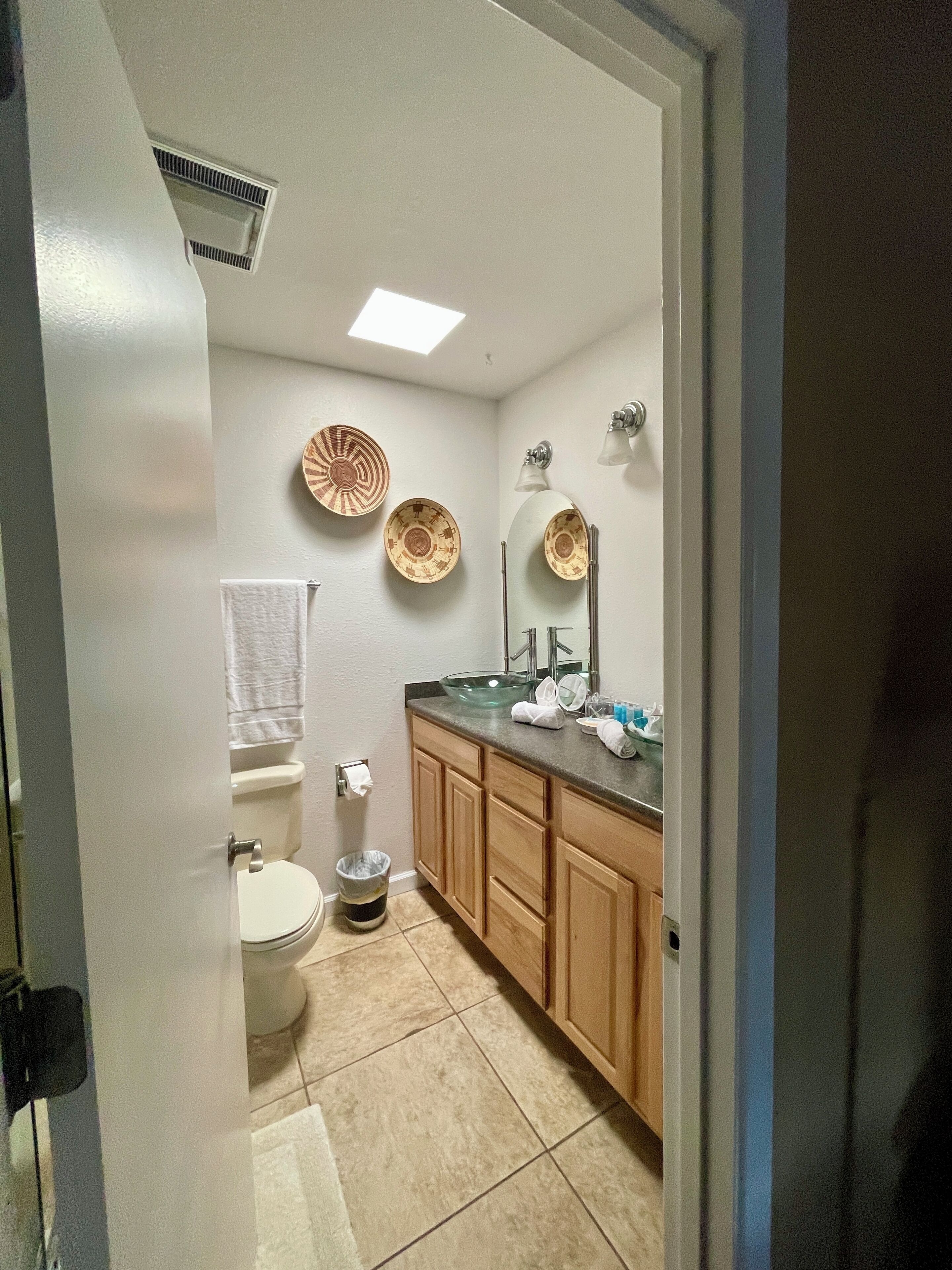 Une salle de bain avec des toilettes, un lavabo et un meuble-lavabo. Des assiettes décoratives sont accrochées au mur et une serviette est suspendue à la porte.