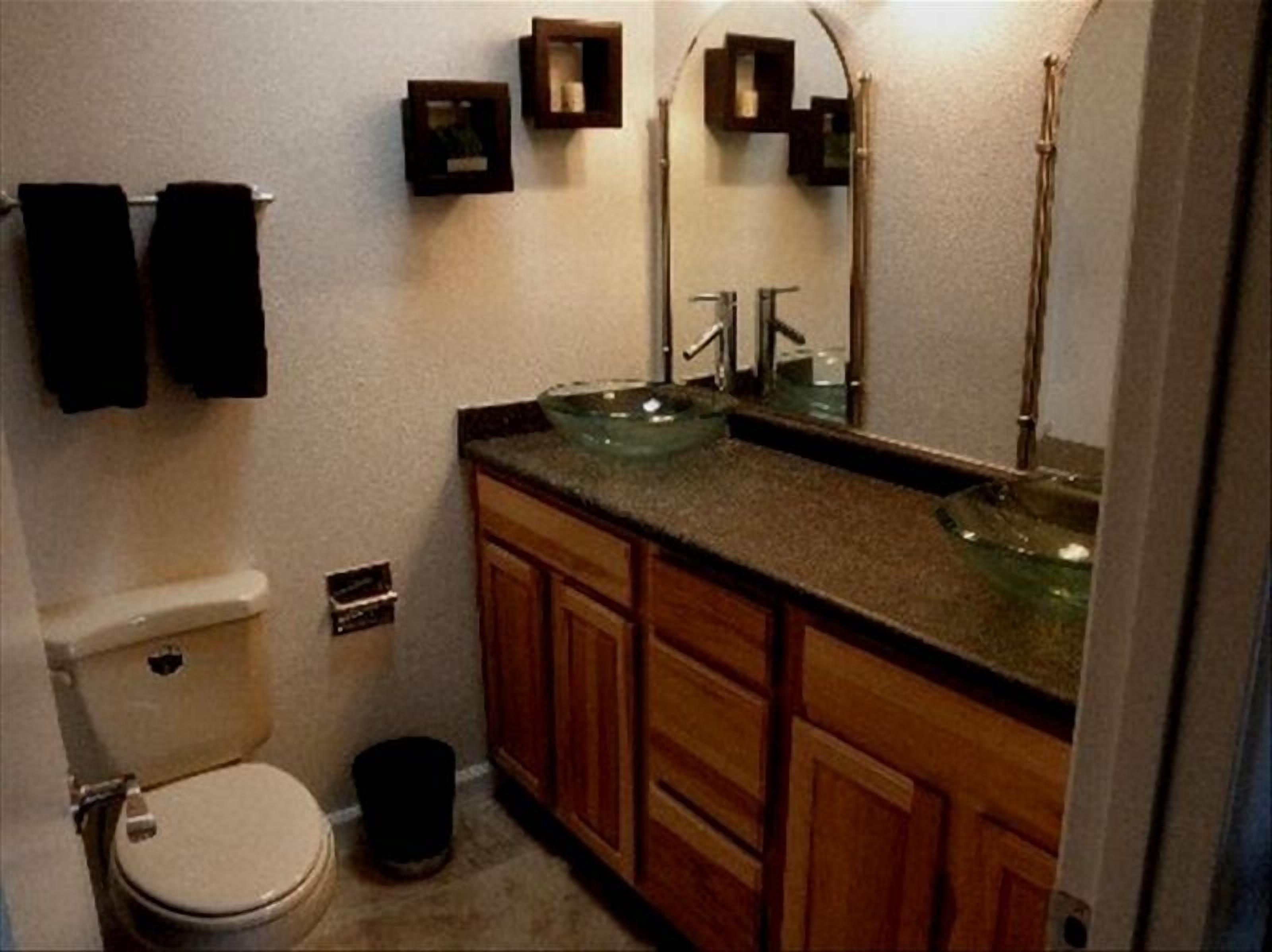 Un baño pequeño con inodoro, lavamanos y espejo. Hay armarios de madera y un cesto de basura.