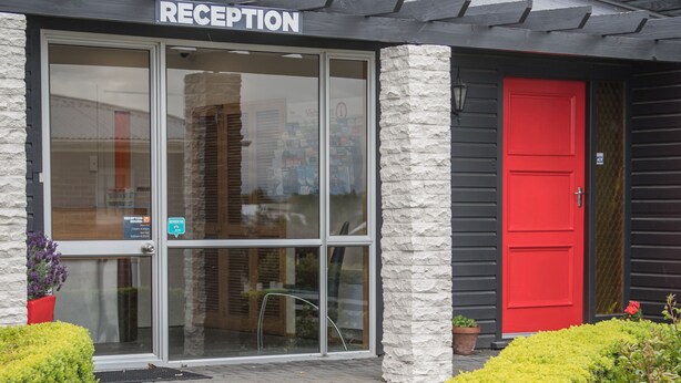 A reception area with a glass door, a red door, and a stone pillar. - Cedar Lodge Motel (Timaru)