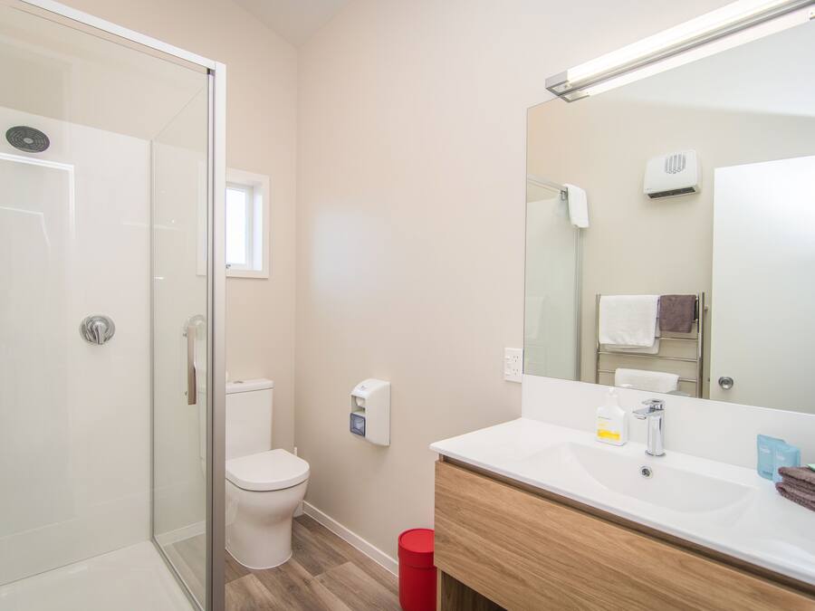 A modern bathroom with a glass shower enclosure, a toilet, a sink with a mirror, and a red trash bin.