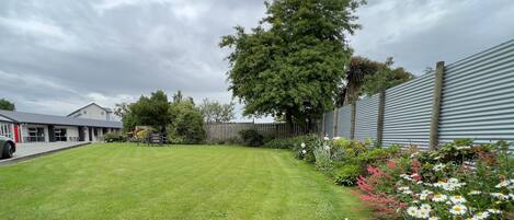 A well-maintained lawn with a wooden bench, a variety of flowers, and a building with a corrugated metal wall in the background.