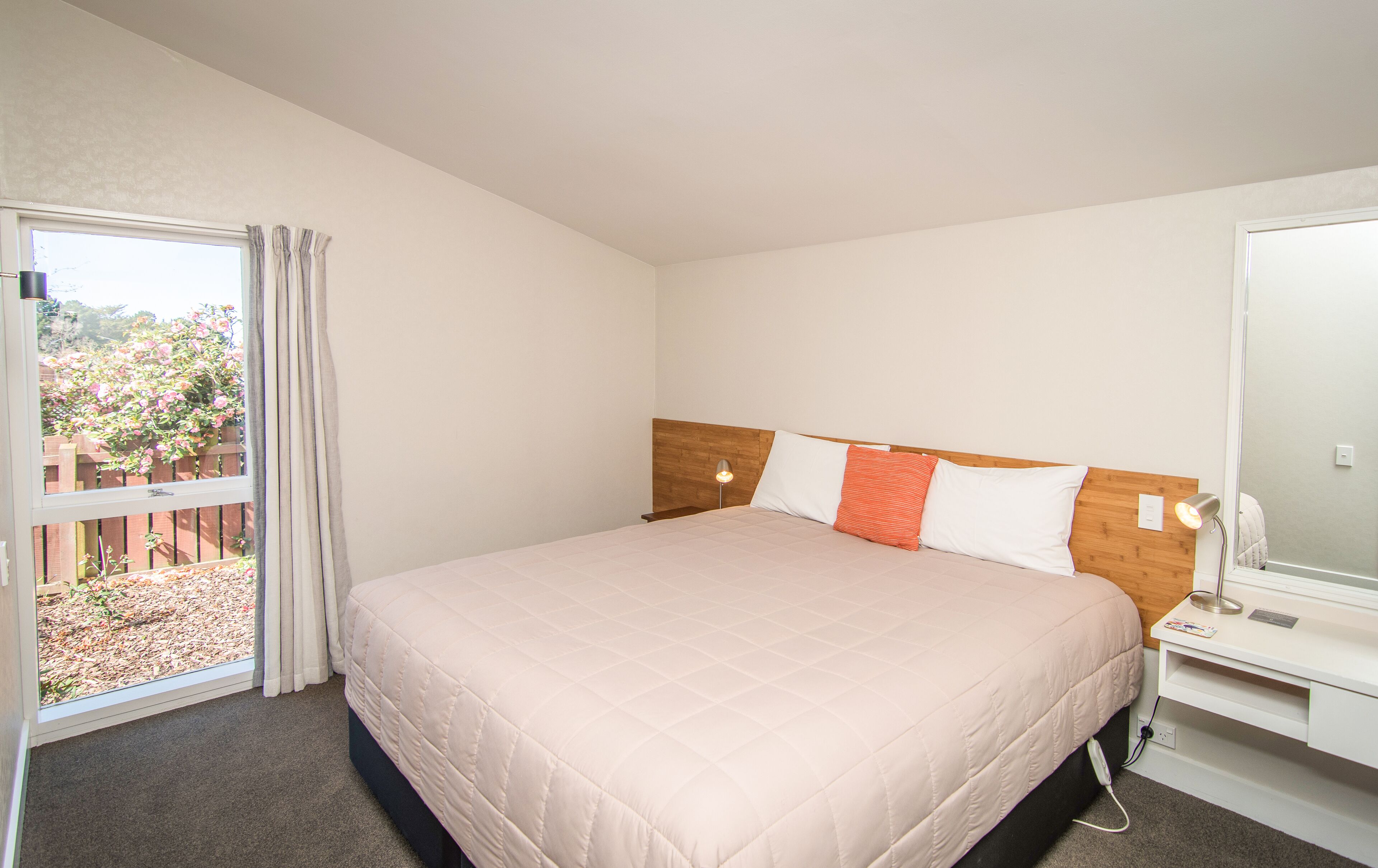 A bedroom with a large bed, a bedside table, a lamp, and a window with curtains.