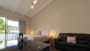 A room with a bed, a desk with a laptop, a leather sofa, and a window with curtains. - Cedar Lodge Motel (Timaru)