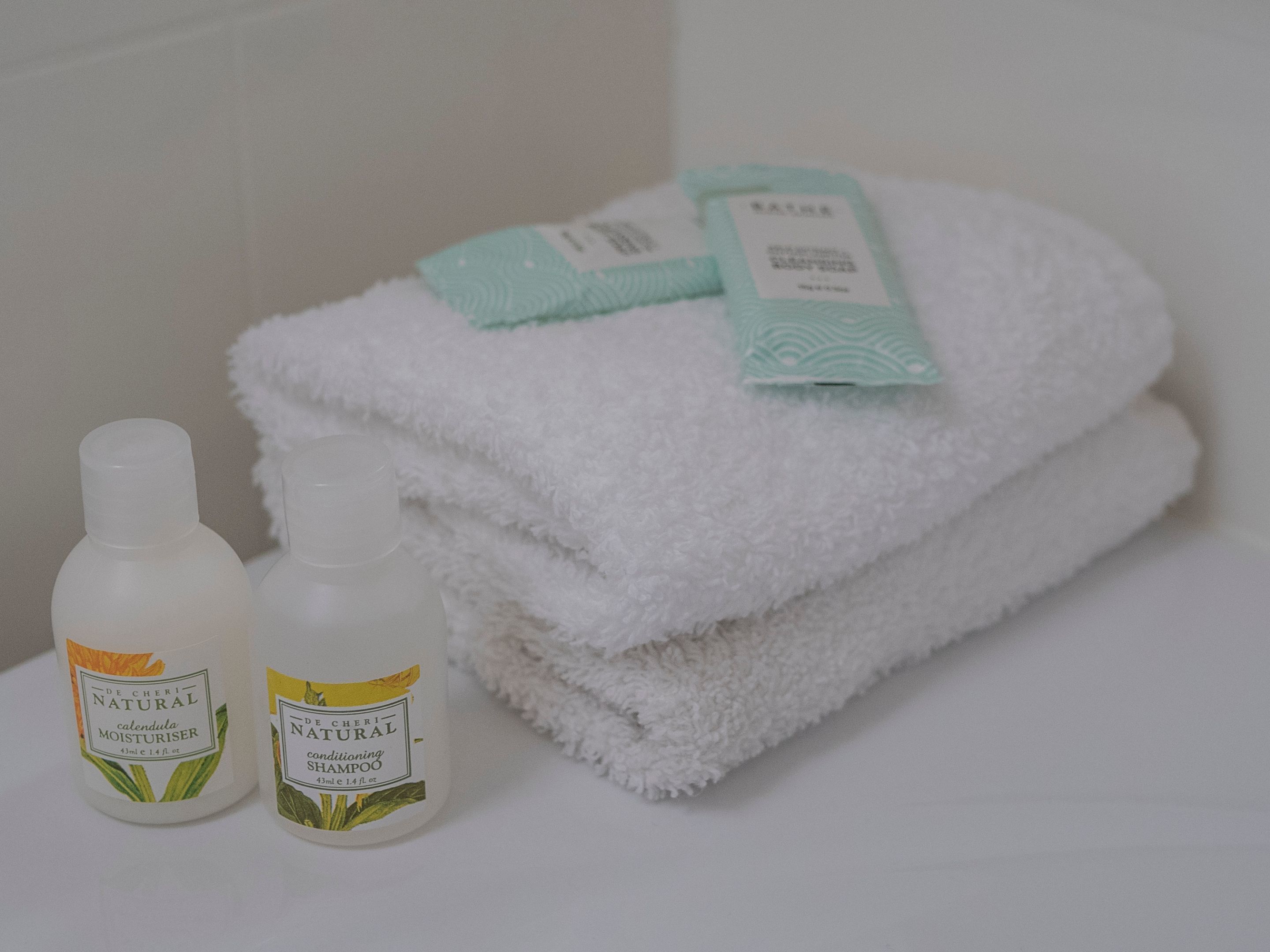 Ein Badezimmer mit einem weißen Handtuch auf einem Regal, zwei Flaschen von De Cheri Natural Produkten und einem grünen Handtuch mit Etikett.