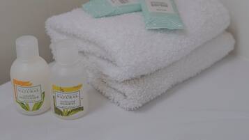 Ein Badezimmer mit einem weißen Handtuch auf einem Regal, zwei Flaschen von De Cheri Natural Produkten und einem grünen Handtuch mit Etikett.