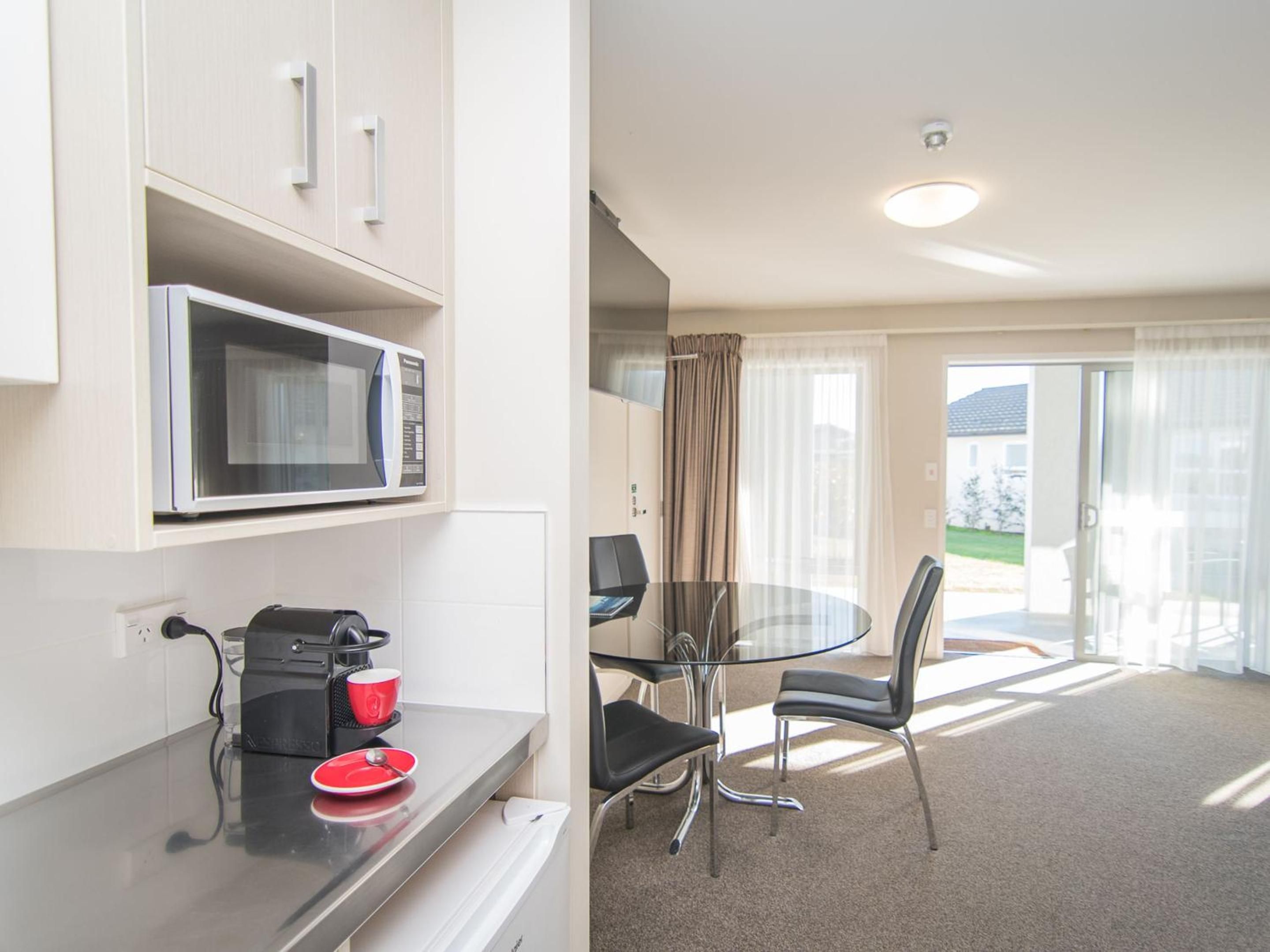 A compact kitchenette with a microwave, coffee maker, and a small dining area with a glass table and chairs.