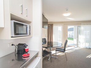 Una kitchenette compacta con microondas, cafetera y un pequeño comedor con mesa y sillas de vidrio.