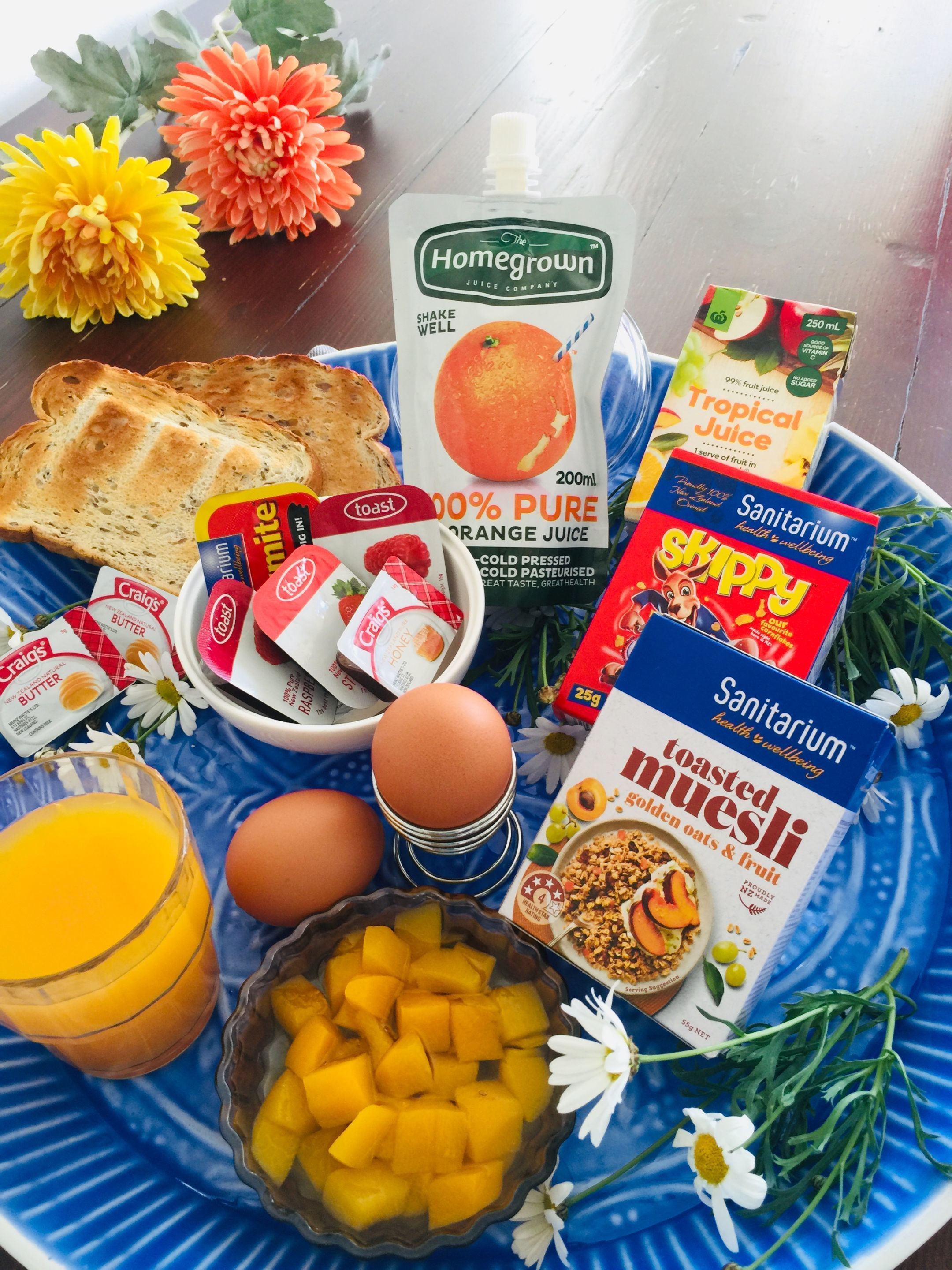 A breakfast tray with toast, orange juice, cereal, eggs, and a bowl of fruit.