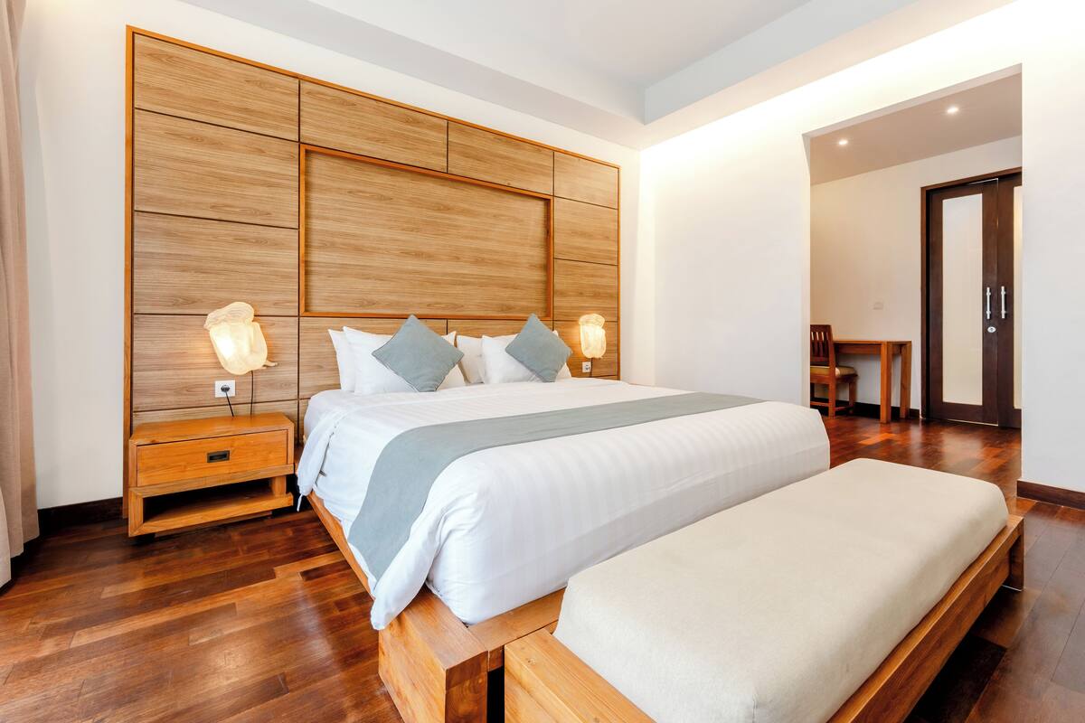 A modern bedroom with a large bed, wooden headboard, bedside tables, and a bench.