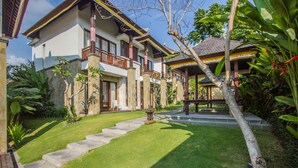 A two-story house with a balcony, surrounded by a well-maintained garden with a stone pathway leading to the entrance.