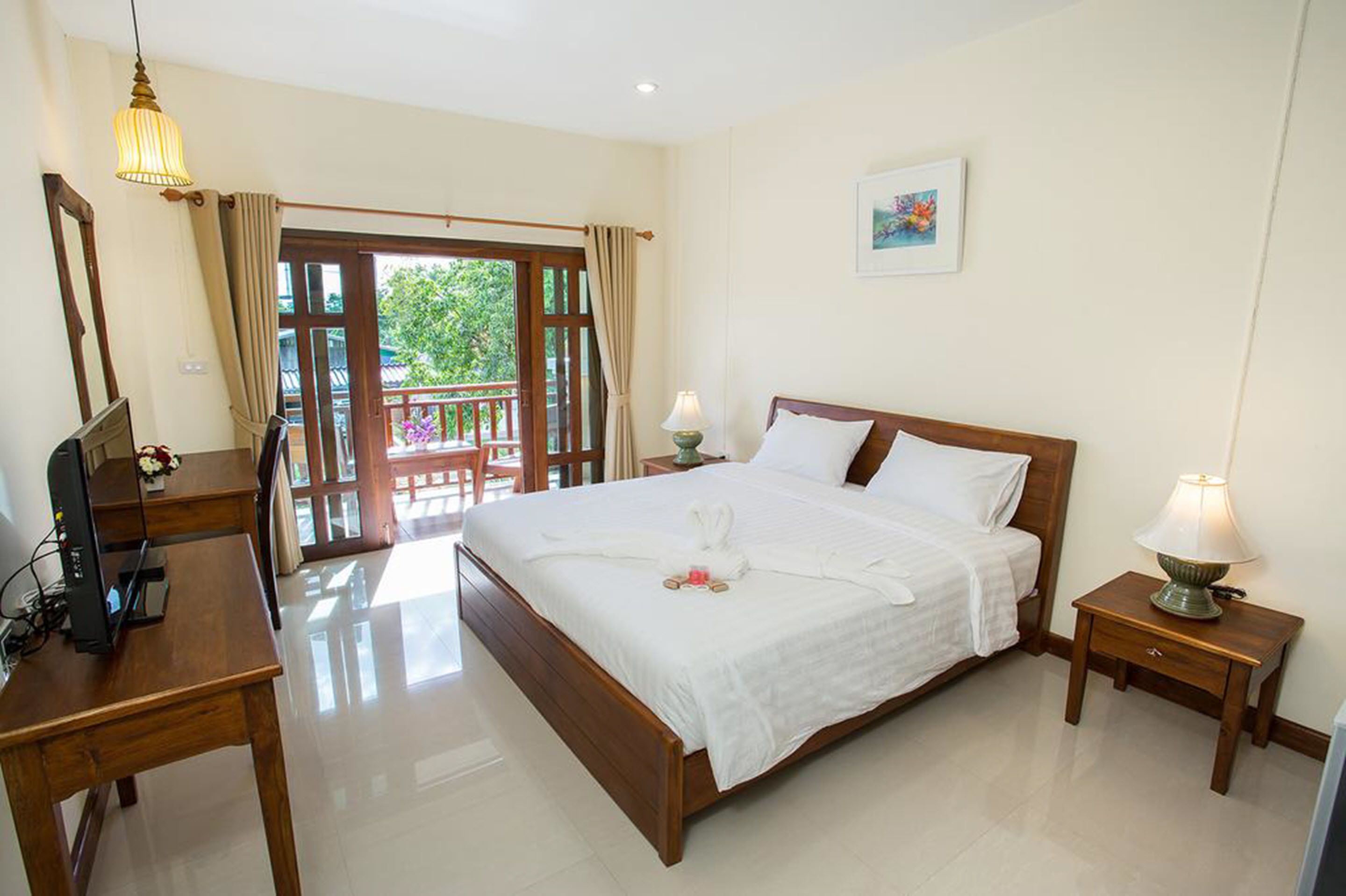 A hotel room with a wooden bed, a desk with a computer, a lamp, and a view of a balcony.