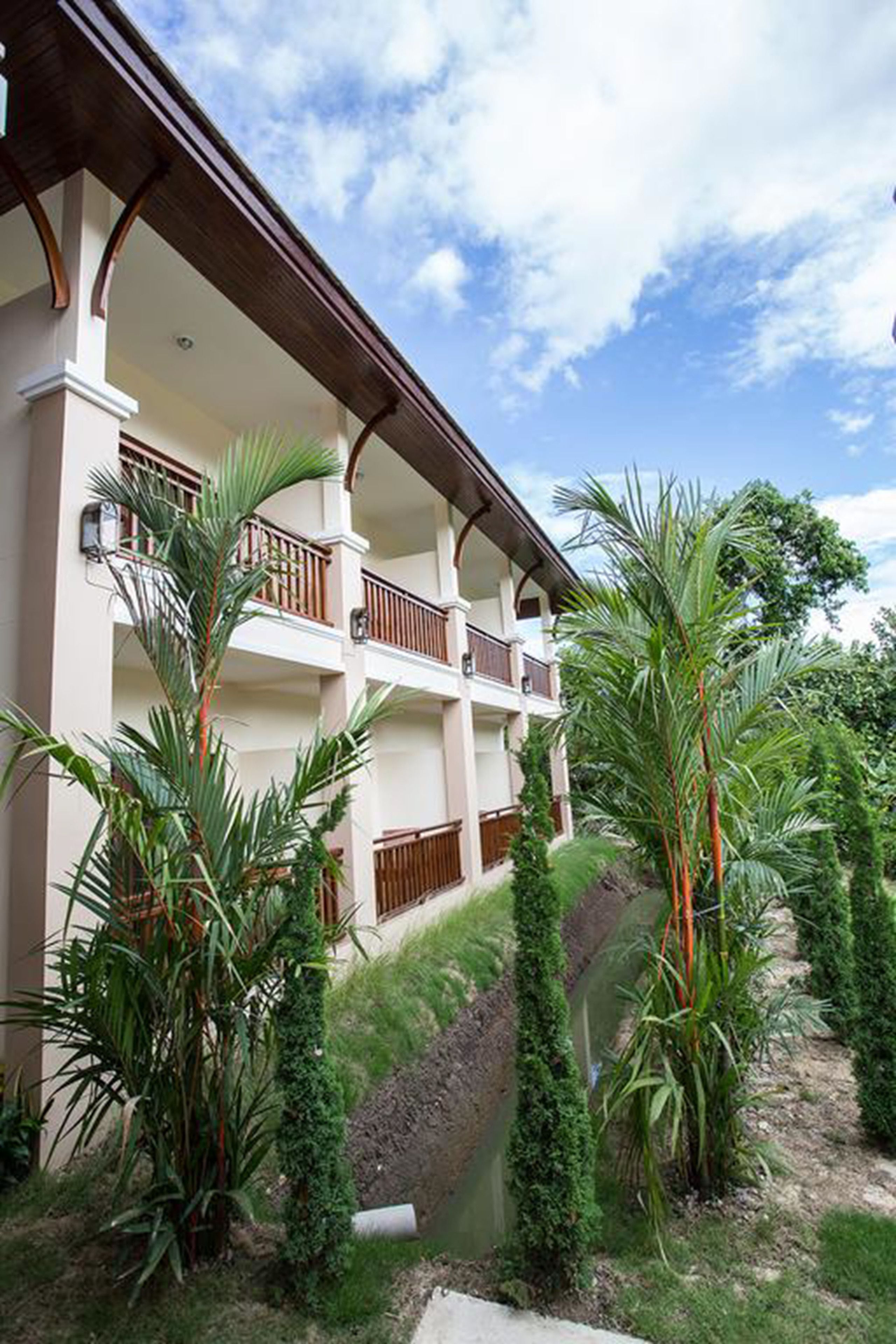 Un hotel de varios pisos con balcones, rodeado de exuberante follaje y una pequeña fuente de agua.