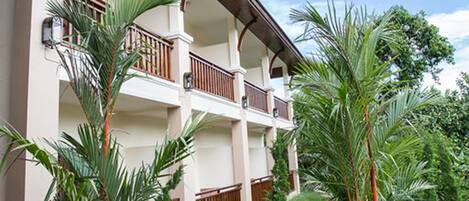 Un hotel de varios pisos con balcones, rodeado de exuberante follaje y una pequeña fuente de agua.