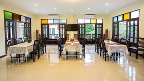 A spacious dining area with multiple tables and chairs, large windows with decorative glass panes, and ceiling lights. - Oh Amphawa Boutique Resort (Amphawa)