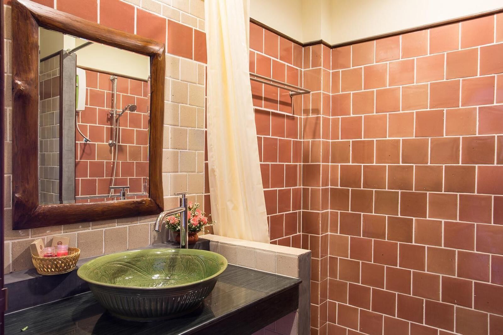 A bathroom with a green ceramic sink, a mirror, a shower with a glass door, and red-tiled walls.
