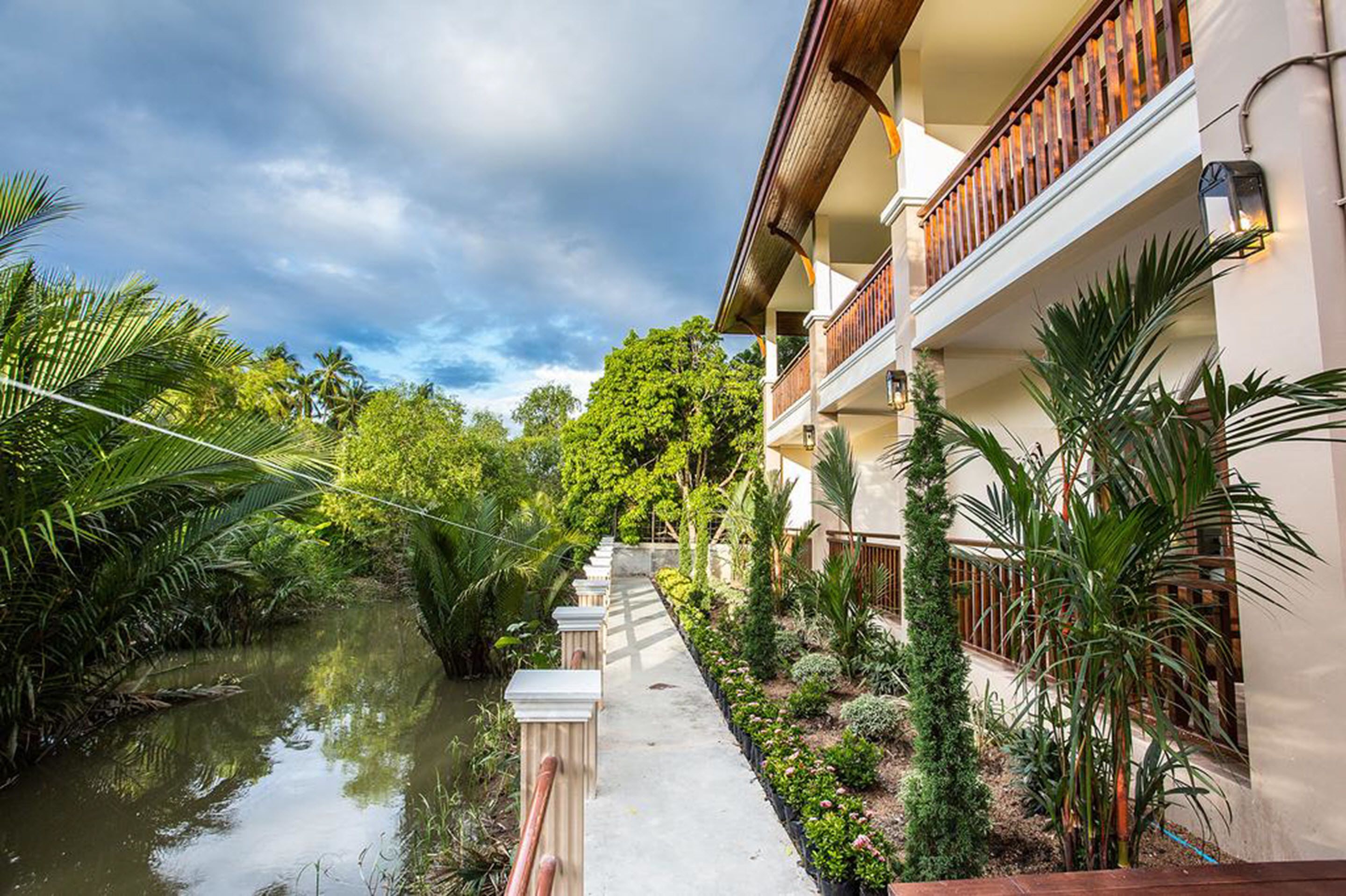 A hotel with a water canal, lush greenery, and a balcony with wooden railings.