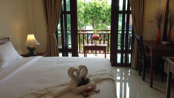 A hotel room with a bed, a nightstand with a lamp, a table with flowers, and a view of the outdoors.