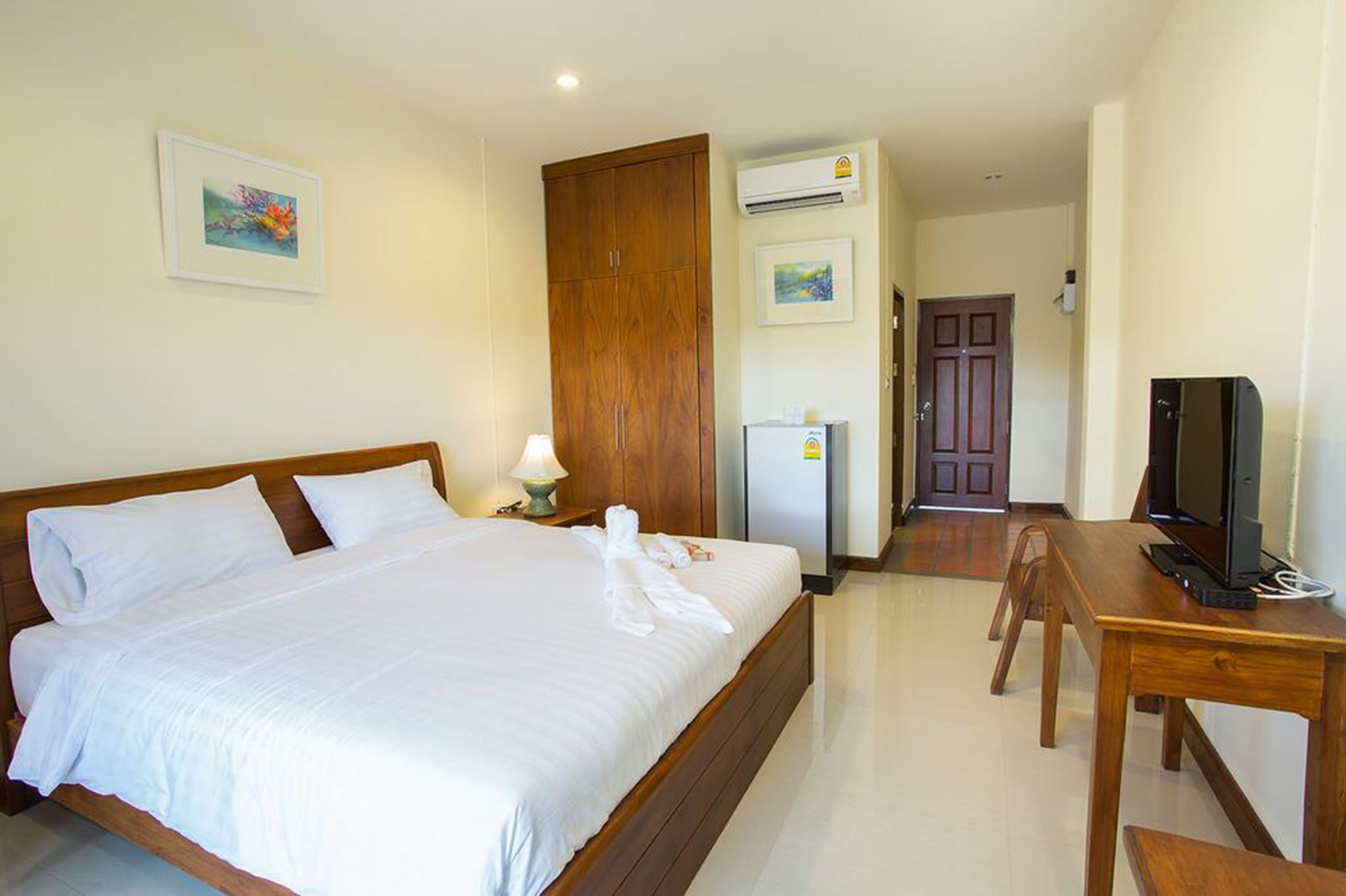 A hotel room with a large bed, a wooden wardrobe, a desk with a television, and a refrigerator.