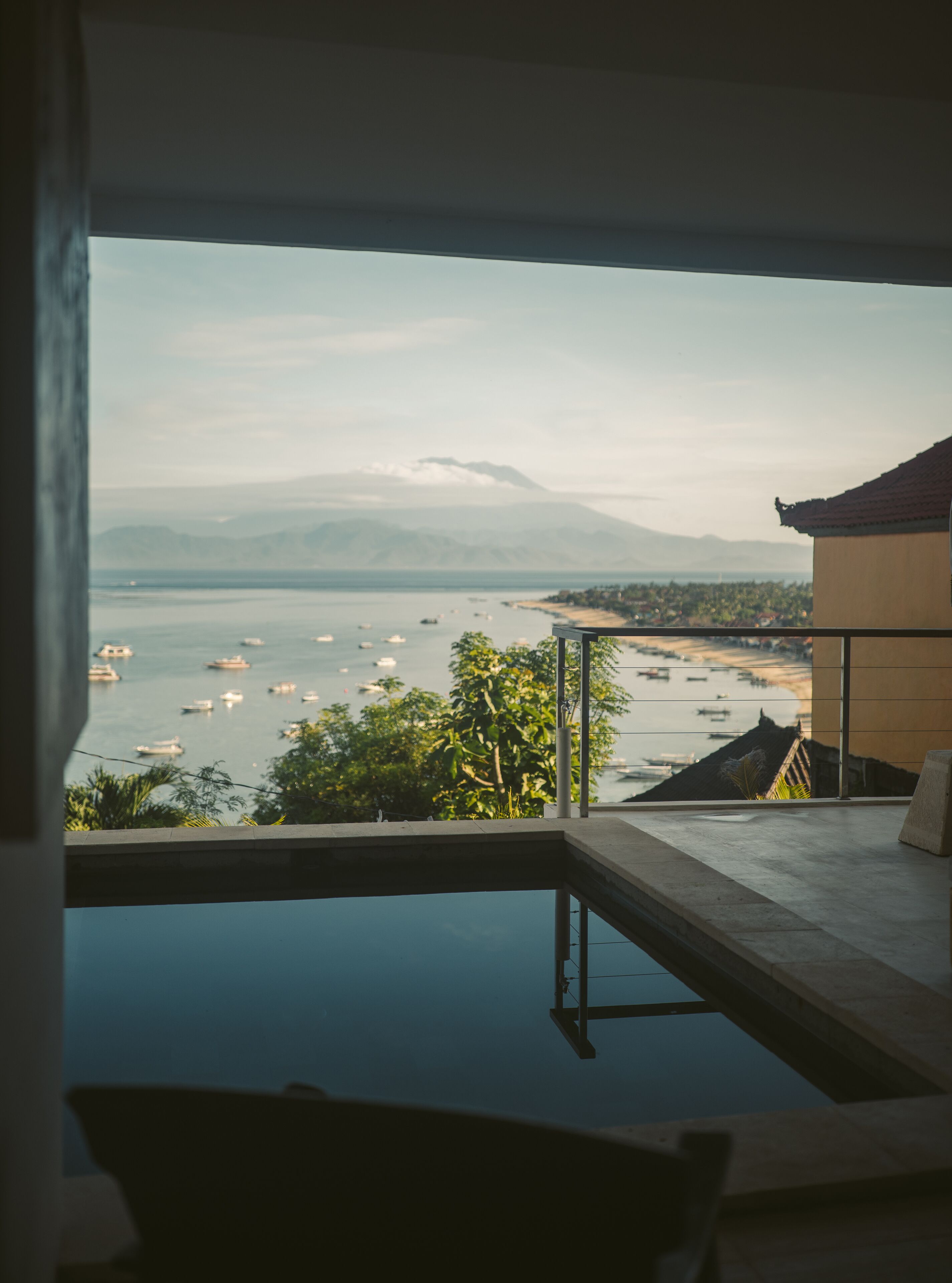 Blick vom Balkon auf ein Gewässer mit Booten, ein Berg in der Ferne und ein Gebäude mit einem Ziegeldach.