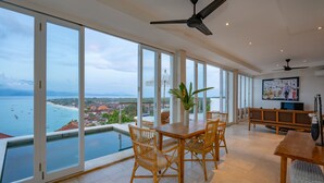 A spacious room with a large dining table and chairs, a ceiling fan, and a view of the sea through large windows. - Aqua Nusa - Boutique Lembongan Villas (Lembongan Island)