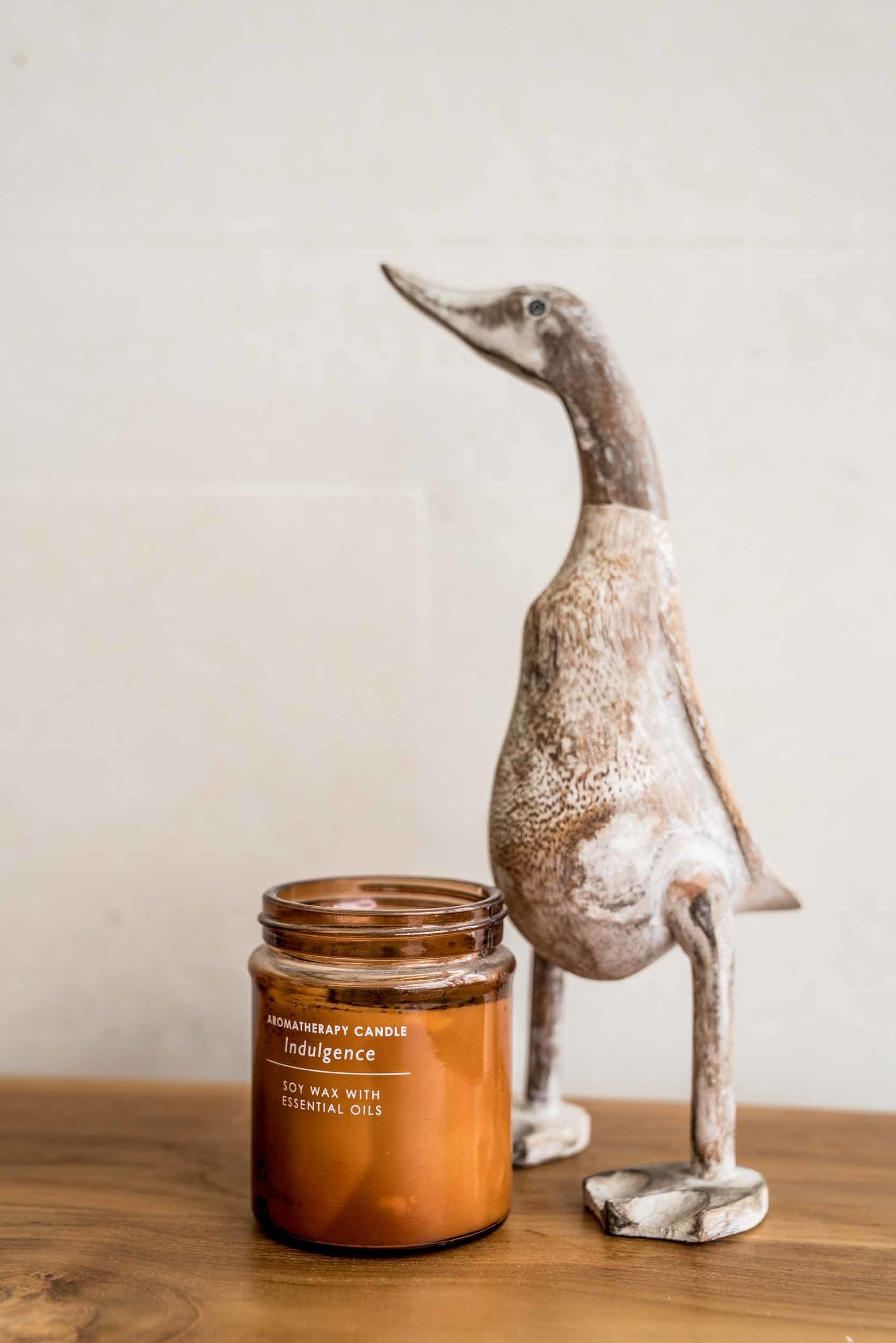 Una vela con el rótulo "Aromatherapy Candle Indulgence" junto a una figura decorativa de un pingüino.