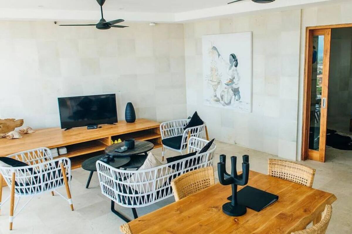 Un salon moderne avec une table à manger en bois, des chaises en osier blanches, un téléviseur à écran plat et un tableau accroché au mur.