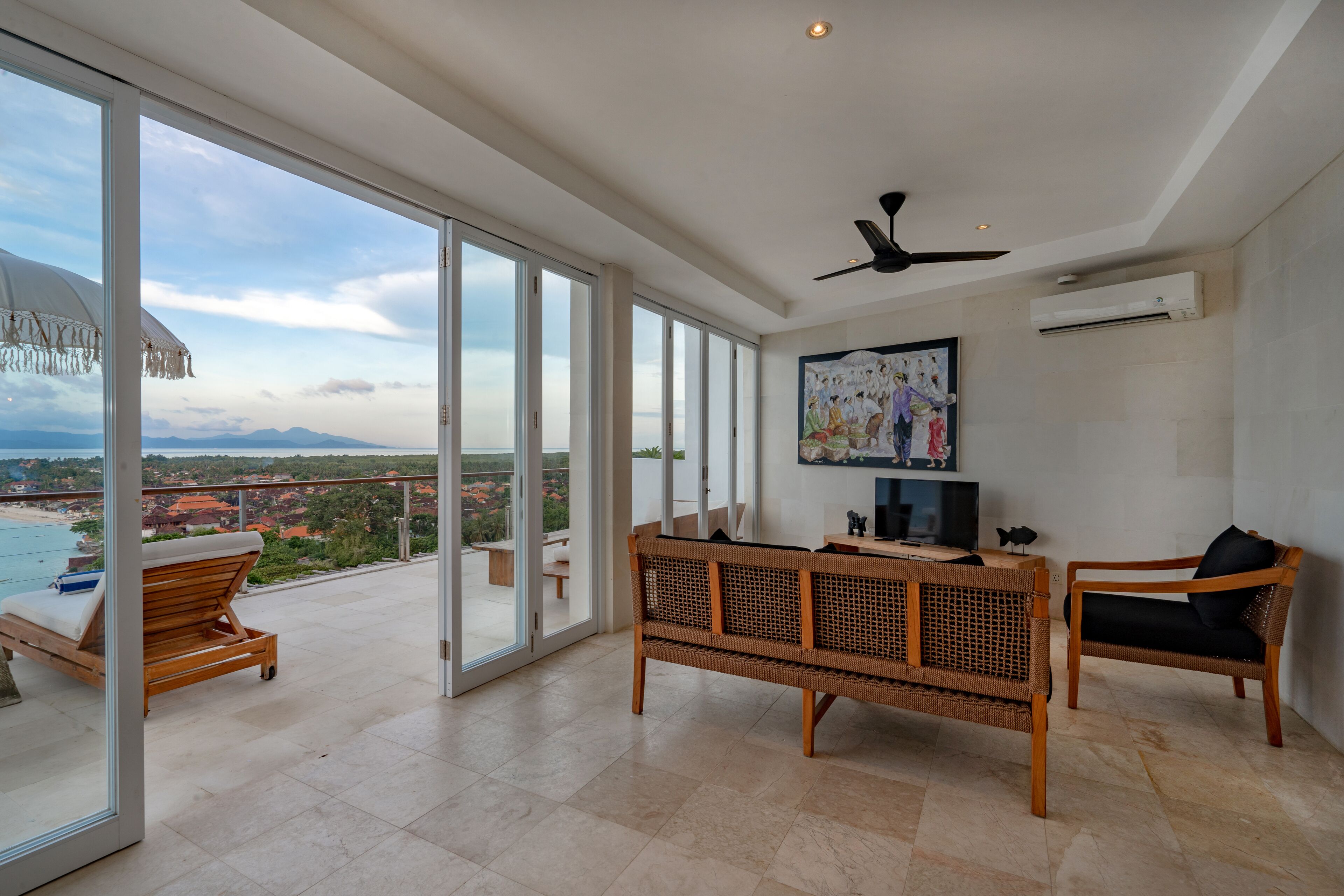 Un ampio balcone con vista sul mare e sulle montagne, arredato con un divano, sedie e un tavolino.