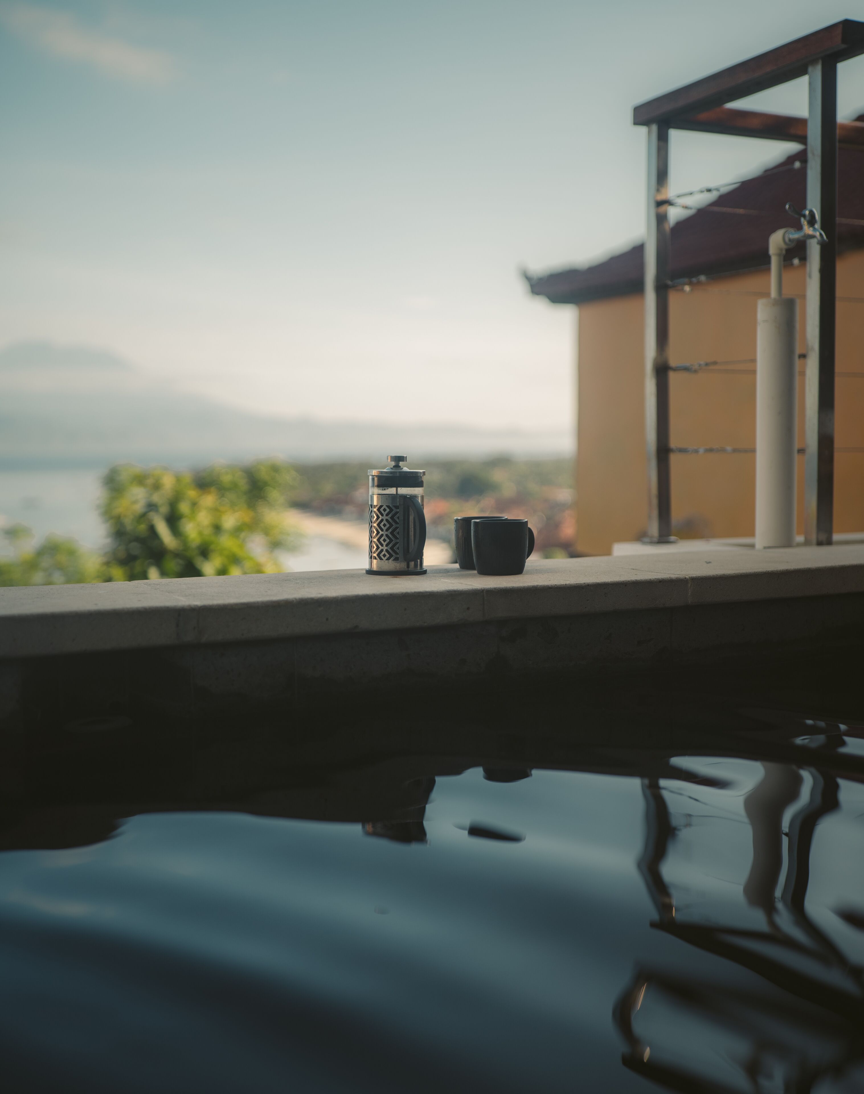 A pool with a coffee maker and cups on a ledge, overlooking a scenic view.