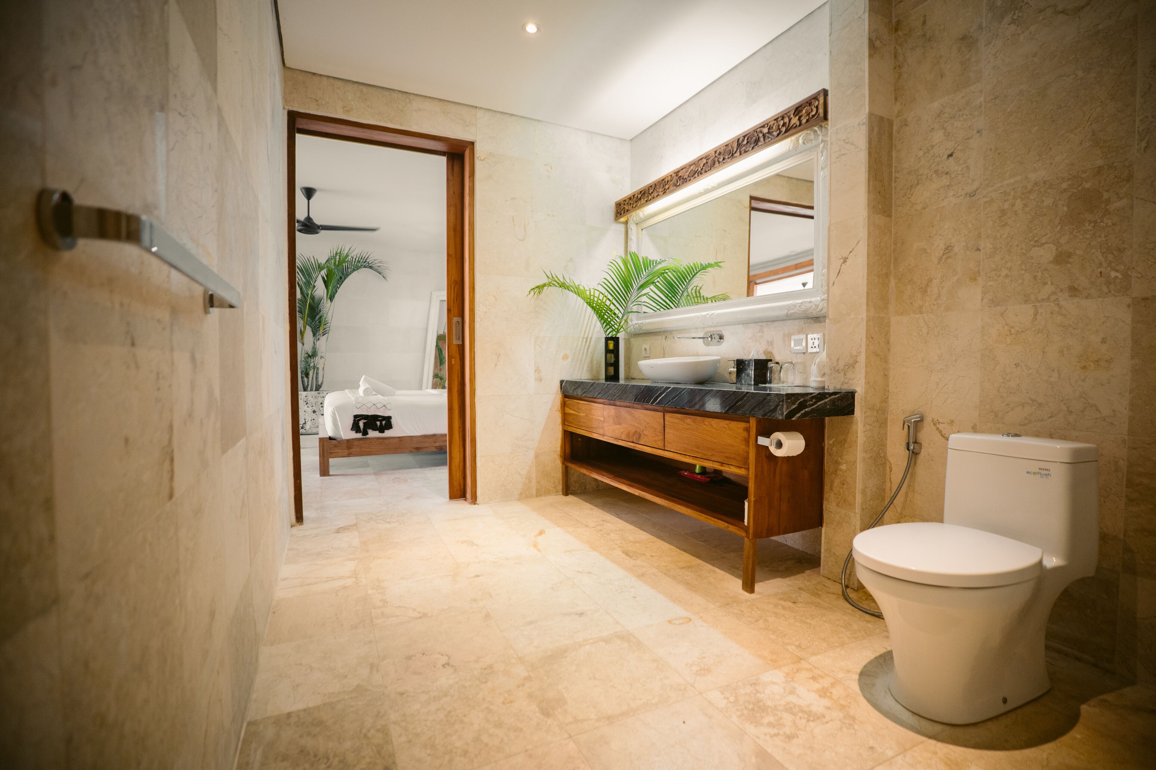 A modern bathroom with a marble floor, a wooden vanity, a white toilet, and a large mirror.