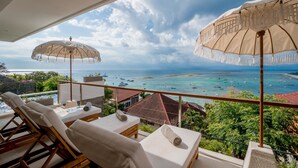 A balcony with two lounge chairs and a table, overlooking a coastal view with boats and greenery. - Aqua Nusa - Boutique Lembongan Villas (Lembongan Island)