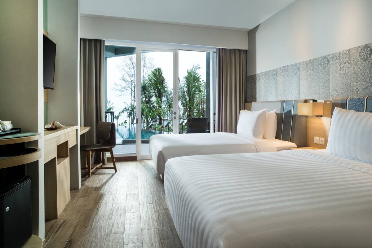 Habitación de hotel con dos camas, un escritorio, una silla y vista a una piscina.