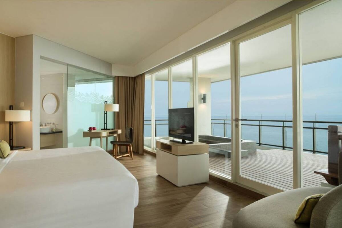 Habitación de hotel moderna con una cama grande, un escritorio, un televisor y un balcón con vista al mar.