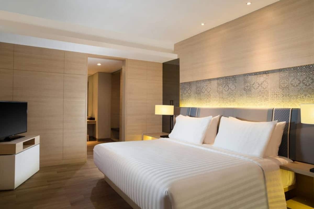 Una habitación de hotel moderna con una cama grande, lámparas de noche, un televisor y un papel tapiz estampado.