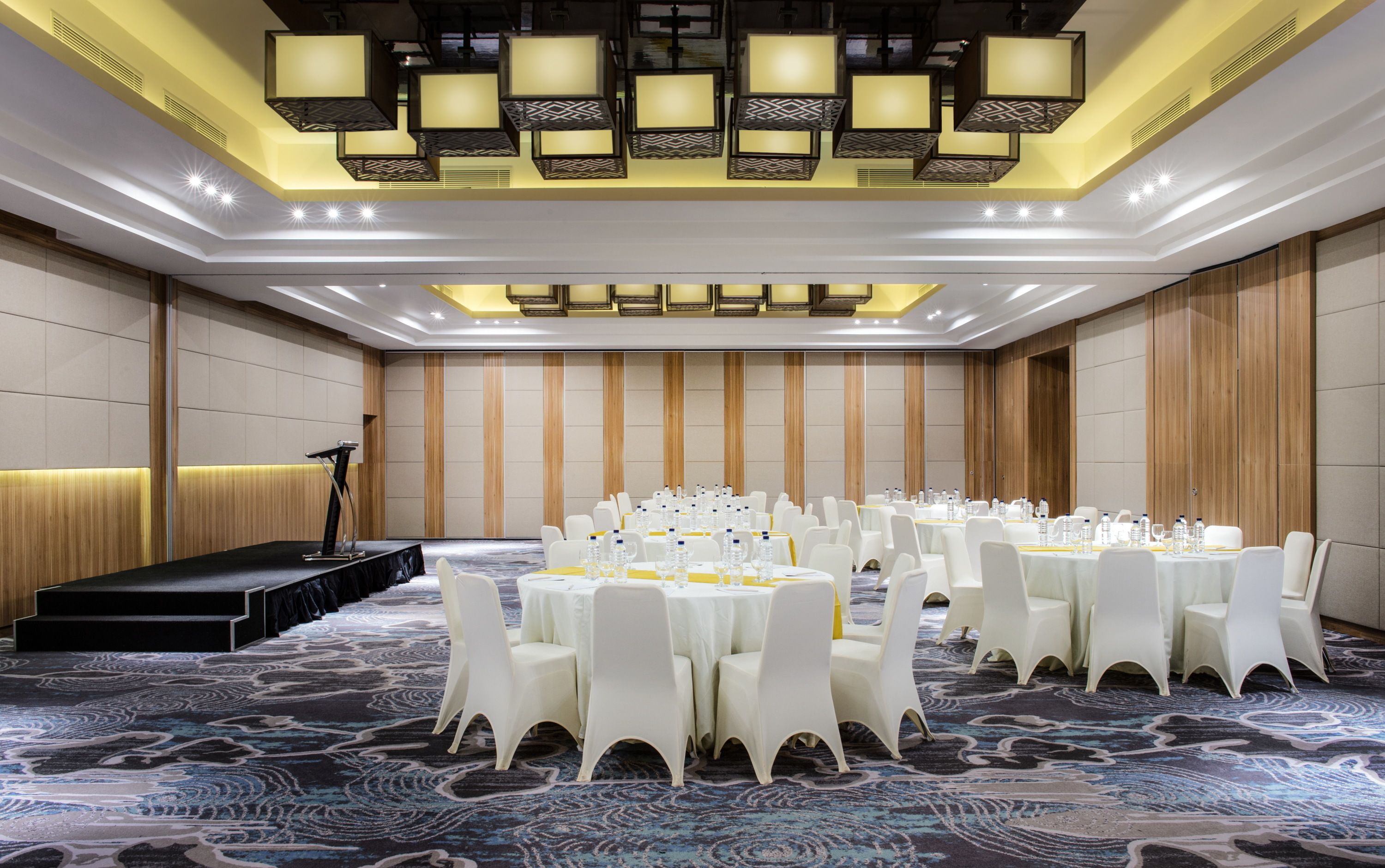 A conference room with round tables, white chairs, and a stage with a podium.