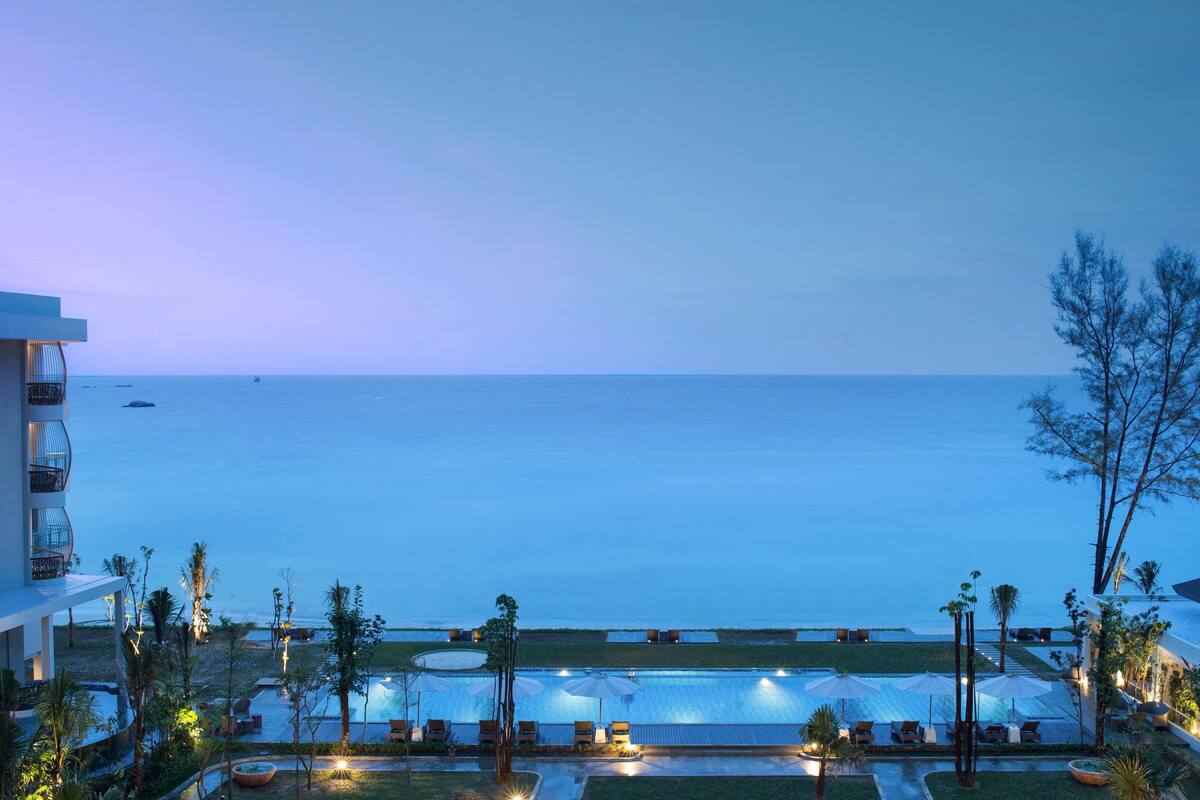 Zona de piscina en un resort con sillones y sombrillas, con vista al mar tranquilo.