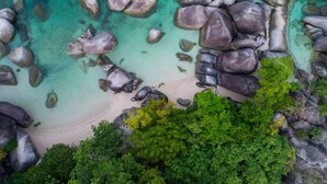 Ein Strand mit klarem türkisblauem Wasser, großen Felsen und üppiger grüner Vegetation.